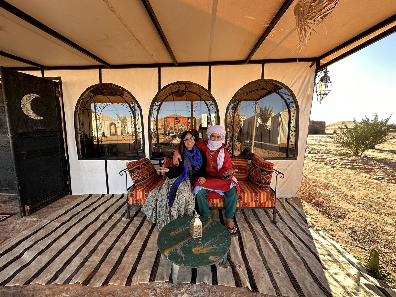 A traveler sitting with a local guide at a luxury desert camp in Morocco. Visit Morocco in December for an unforgettable Sahara experience.