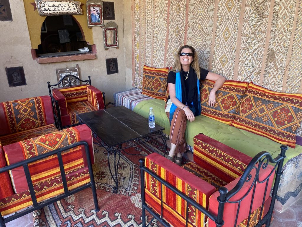 A traveler relaxing in a traditionally decorated Moroccan seating area with colorful Berber cushions and rugs. Visit Morocco in December for authentic cultural experiences.