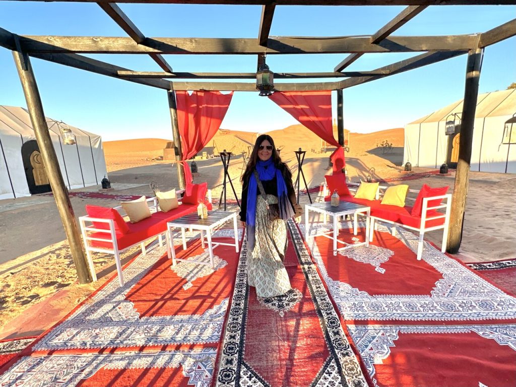 A traveler standing in a luxury desert camp with elegant red and white decor in the Moroccan Sahara. Visit Morocco in January for an unforgettable glamping experience.