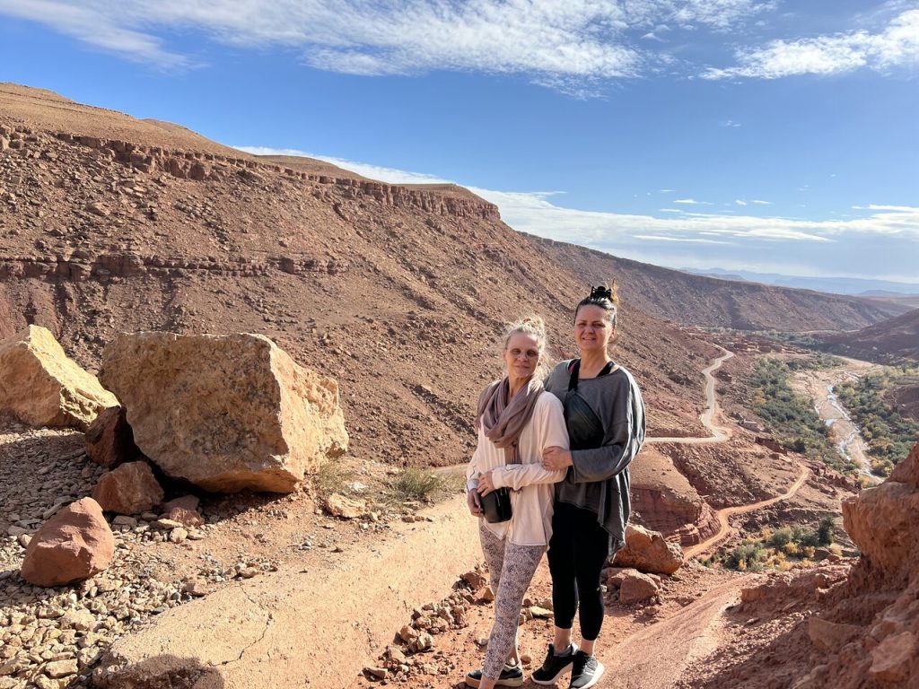 Two travelers standing on a scenic viewpoint overlooking a rocky valley in Morocco. Visit Morocco in December for breathtaking desert landscapes.