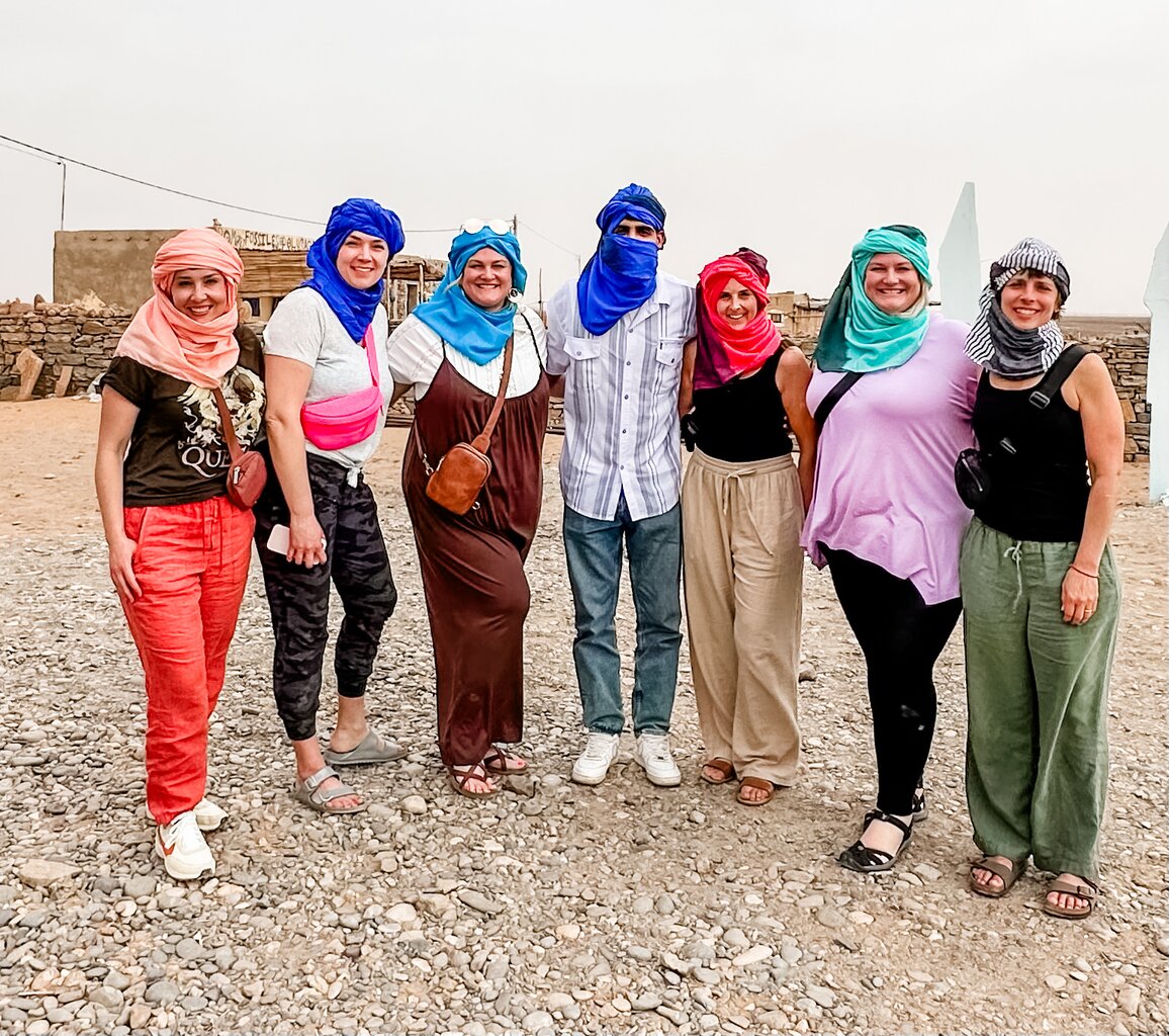 A group of travelers wearing colorful turbans posing in a Moroccan desert village. Visit Morocco in January for an unforgettable desert adventure.